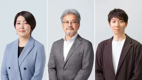 Nintendo The three-dimensional image shows three people in smart clothes facing a blurry background in a technical way. On the left, a clean-cut woman with short dark hair is wearing a light blue suit jacket over a black top. In the middle is a man with glasses, gray hair and a beard wearing a gray suit as he smiles gently. On the right a young man with medium length black hair wears a brown blazer over a white t-shirt. 