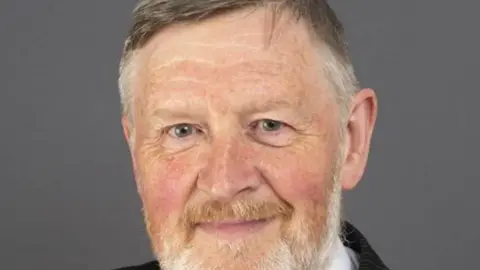 Aberdeenshire Council Councillor David Keating - a man with grey hair and a reddish beard - in front of a grey backdrop