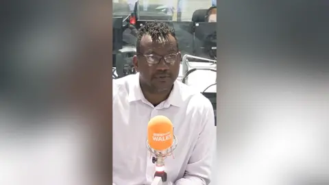 Joseff Gnagbo in a radio studio in a pink shirt with an orange microphone