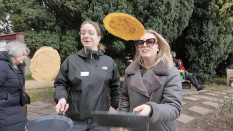 Two girls flipping pancakes with a frying pan.