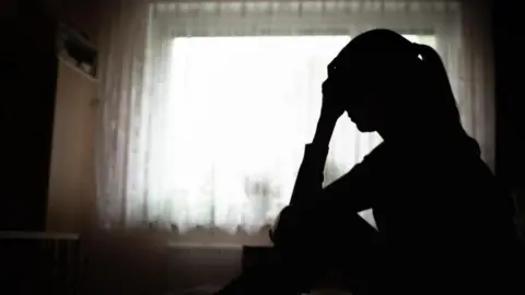 Silhouette of woman holding head in front of net curtains at window