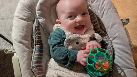 Family handout A photo of healthy baby Riley, holding a toy and smiling.