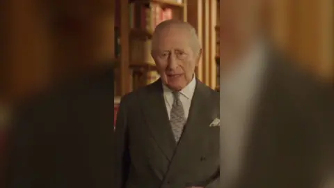 King Charles is wearing a grey suit with a white shirt and a lighter grey tie
