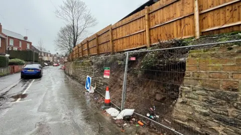 A damaged section of the wall surrounded by metal fencing.