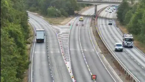 National Highways Part of a motorway is closed off and a police car is parked on it.