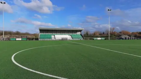 Victoria Park Guernsey FC's new stadium Victoria Park. It has a 3G pitch and a stand in the distance with green and white seats.