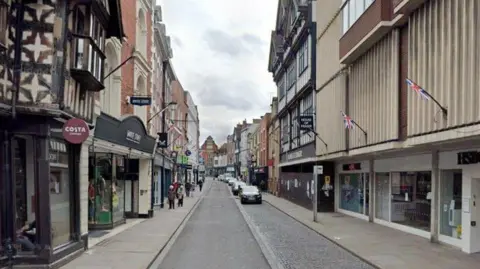 BBC A generic shot along a town centre street with buildings of various ages and designs along both sides. Some cars are parked on the right.