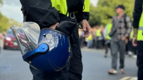 A police officer holds a riot helmet in front of crowds