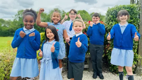 Children smiling and giving a thumbs up 