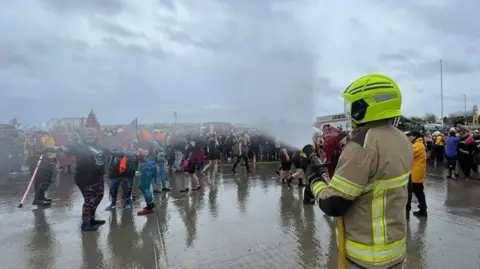 Paul Murphy / BBC A large group of people being hosed by a fireman as part of the charity event