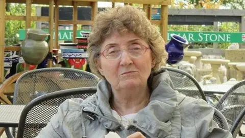 Family photograph Pat sitting outside at a garden centre cafe wearing a green coat 