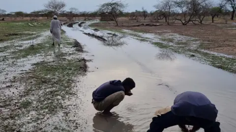 Mohamed Zakaria Two men crouch over a pool of rainwater in the road as the travel out of Sudan
