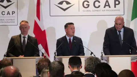 Wes Streeting (centre) speaks at a podium