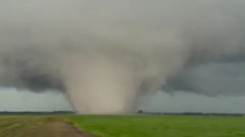 A large tornado is seen moving across a green field in a vertical photo