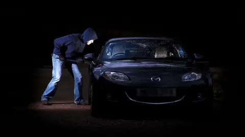 A man breaking into a parked car at night. 