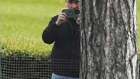 Man films from behind a tree