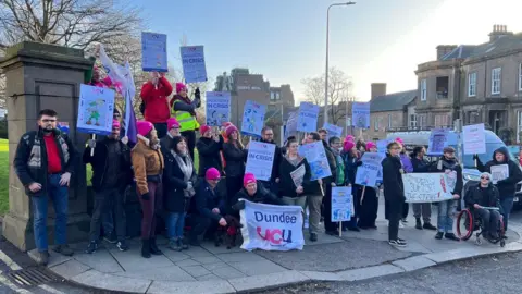 A group of pickets stand on the street waving banners