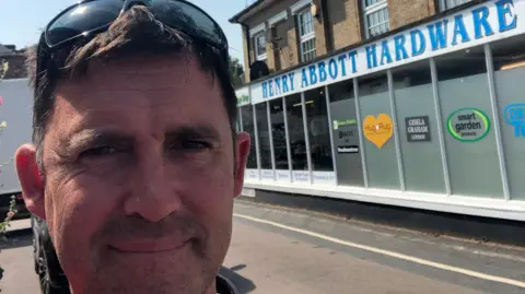 Supplied A selfie-style image of a man who is wearing sunglasses on his head. Behind him is the Henry Abbott Hardware Store.