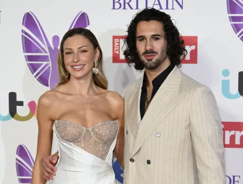 PA Media Zara Mcdermott with Strictly partner Graziano Di Prima. Graziano has his hand on Zara's waist. Both are posing ifnront of Pride of Britain Awards backdrop 
