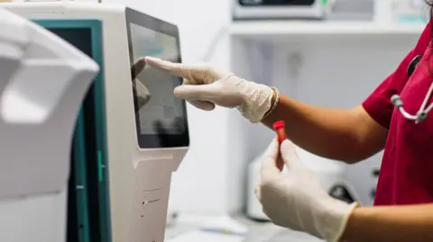 Getty Images A female laboratory technician looks at the results of a blood test on a computer, stock image.