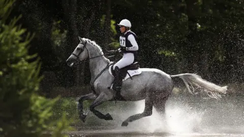 Getty Images Horse rider Georgie Campbell in action in 2022. She is riding a grey horse through water. 