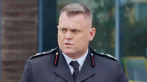 Nathaniel Hooton, deputy chief fire officer at Gloucestershire Fire and Rescue, in his uniform, looking to the side. He has short brown hair and is standing outside.