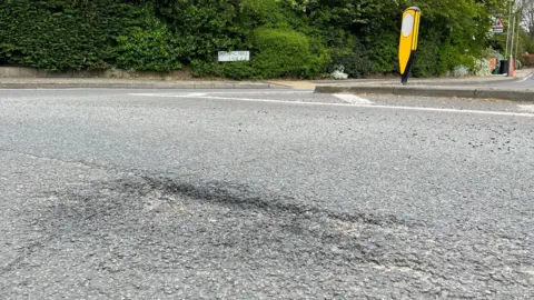 Tom Larsen-Wright/BBC A pothole in the foreground with Patching Hall Lane road sign in the background