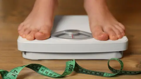 Bare feet on a set of scales with a twirl of green tape measure in the foreground