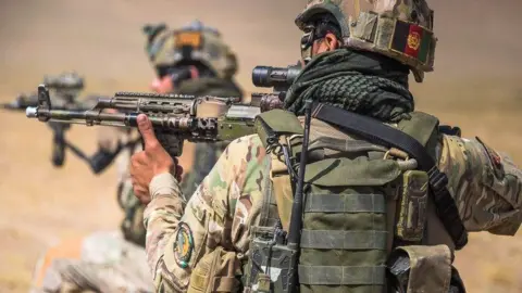 A picture of two soldiers wearing khaki green holding guns, with helmets on