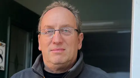 Dean Gosnell has short grey hair and is wearing glasses as he looks at the camera 