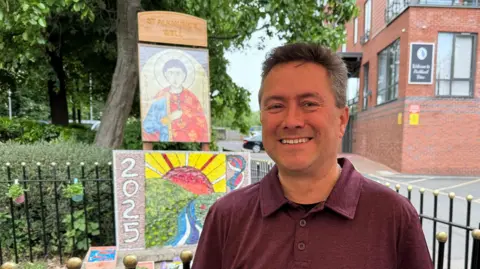 A man stood smiling in front of a newly-dressed well