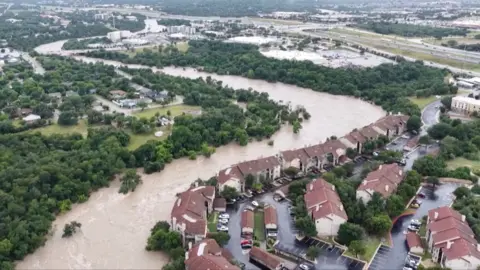 Drone footage shows a swollen river and flooded houses from above