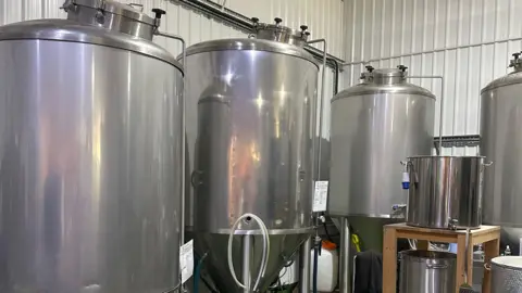 Four steels cylinder-shaped vats in a white-walled warehouse.
