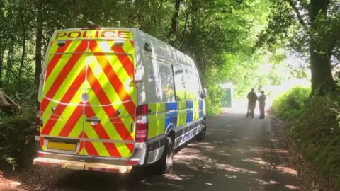 A police van and two officers in a leafy country lane