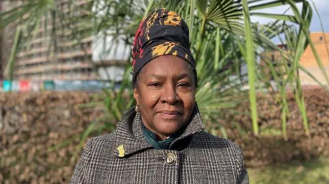 Sherwin is wearing a plaited coat with a children in need badge on her collar. 