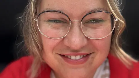 Contributed Close up of a smiling woman. She is wearing glasses and wearing a red cardigan