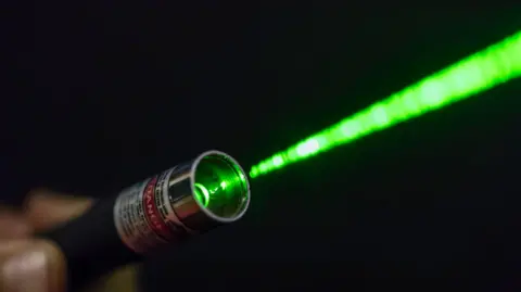A silver laser pointer with a green beam.