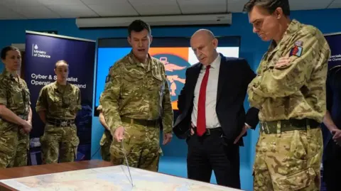 Four military personnel standing around Defence Secretary John Healey as they point to a map