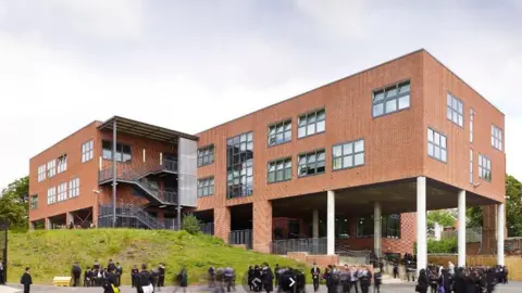 Modern buildings at Moseley School with children in uniform outside in the playground. The building is on columns with an open area underneath and grassy areas around it.