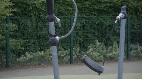 LDRS A children's swing in a playpark. One of the four ropes on the swing is broken.