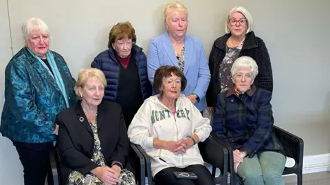 Six older women look solemn as the pose for a photograph together 