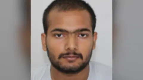 Northamptonshire Police Custody photo of Pankaj Lamba against a grey background. He has dark facial hair, brown eyes and is looking at the camera.