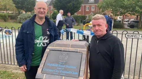 BBC A man wearing a green and black Coventry City T-shirt stood next to the new Coventry City FC granite plaque alongside a man wearing a black jumper.