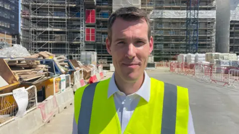 Matthew Pennycook stands on a construction site with a high-volt vest 