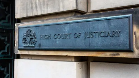 Getty Images A grey metal sign on a brick wall of the court reads: "High Court of Justiciary" in capital letters.