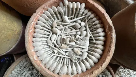 A large ceramic pot filled with unfired clay pipes