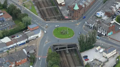 Network Rail An aerial view of the bridge-roundabout on Greek Street in Stockport, with railway tracks seen underneath and homes and roads either side.