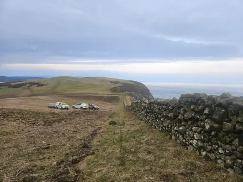 Drummore Coastguard A number of rescue vehicles on grassland next to a dry stone wall on the Solway coast