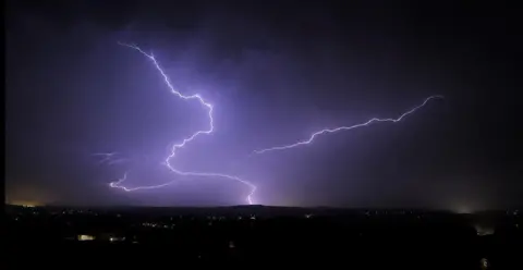 Colby Taylor A bright shaft of lightning striking ground illuminates a dark night sky