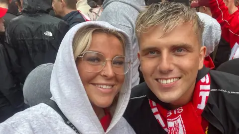 A couple wearing Liverpool gear smile for a selfie in the rain